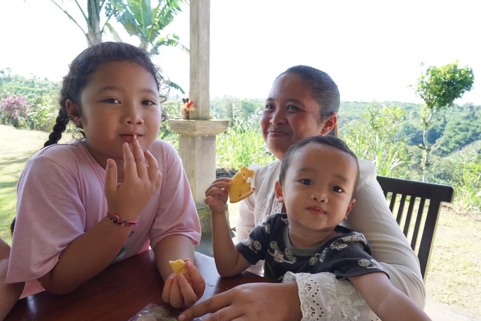 A woman and two children sharing snacks at the table on the veranda, the valley behind them