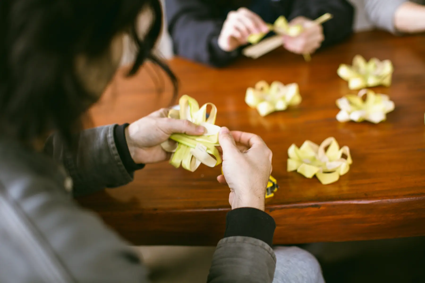 Folding palm leaf into offering trays by hand at a wooden table