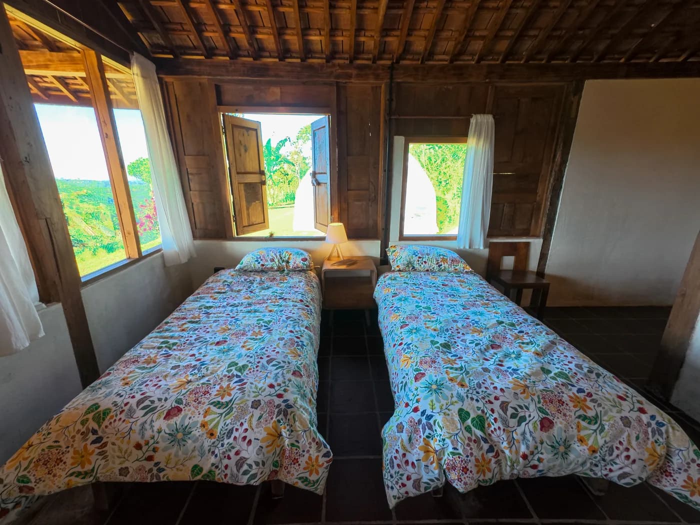 A guest room with two beds, timber walls and windows opening onto the gardens